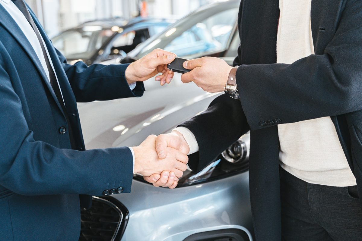 Vendedor entrega a chave de um carro novo ao comprador após fechar negócio na concessionária
