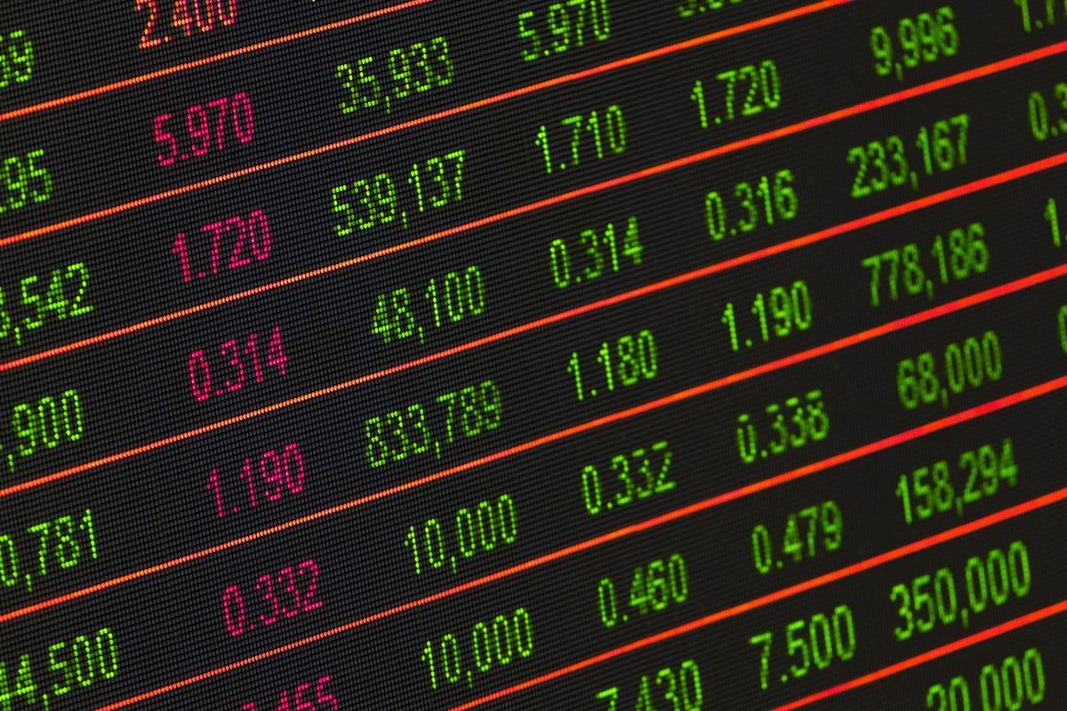 Painel eletrônico de bolsa de valores com cotações em verde, vermelho e rosa, estilo pregão