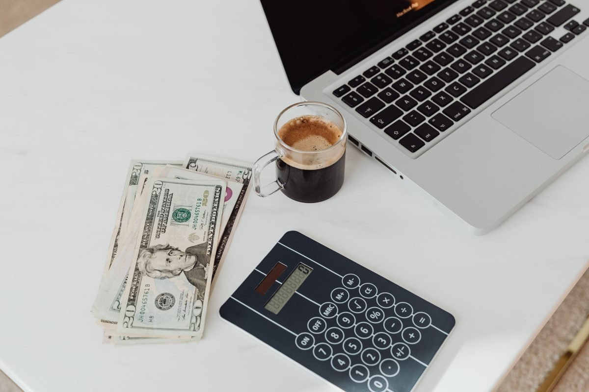 Dinheiro, calculadora, café e notebook sobre uma mesa representando controle de orçamento doméstico