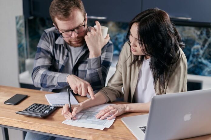 Casal analisando documentos financeiros e calculadora em mesa de cozinha, avaliando decisão de crédito