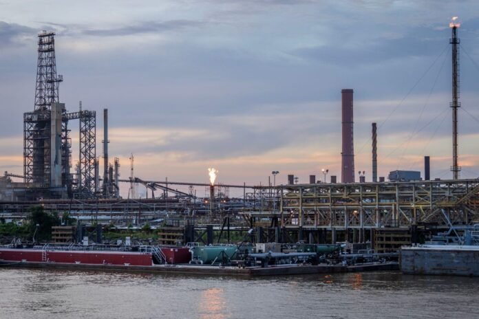 Refinaria de petróleo industrial à beira de um rio, com torres e chaminés ao entardecer