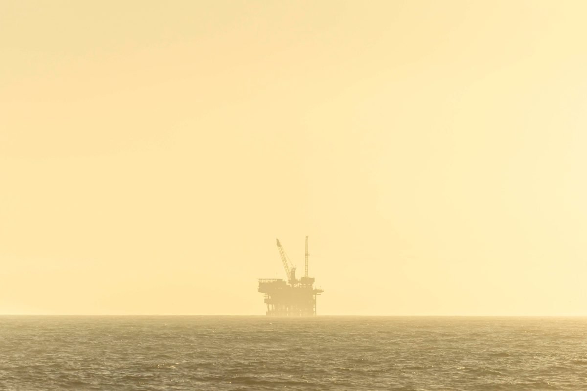 Plataforma de petróleo offshore silhuetada contra o céu dourado do entardecer, simbolizando o choque energético