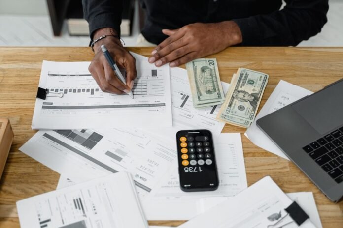 Pessoa analisando relatórios financeiros impressos sobre uma mesa, com calculadora no celular e notebook ao lado, para comparar opções de investimento