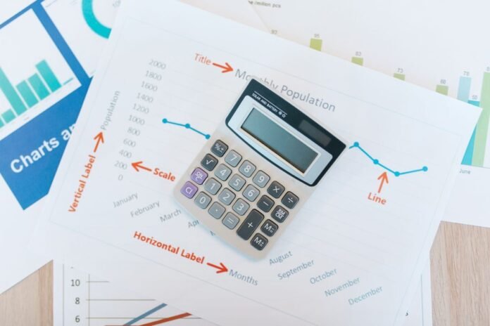 Calculadora sobre folhas impressas com gráficos de linhas e barras em uma mesa de madeira