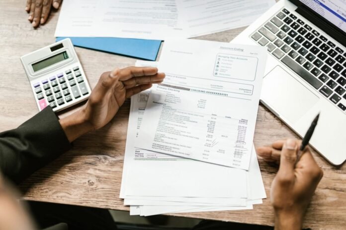 Vista de cima de duas pessoas à mesa analisando extratos e documentos financeiros, com calculadora e notebook ao lado