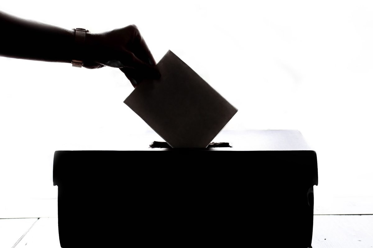 Silhueta de mão depositando voto em urna, simbolizando o processo eleitoral