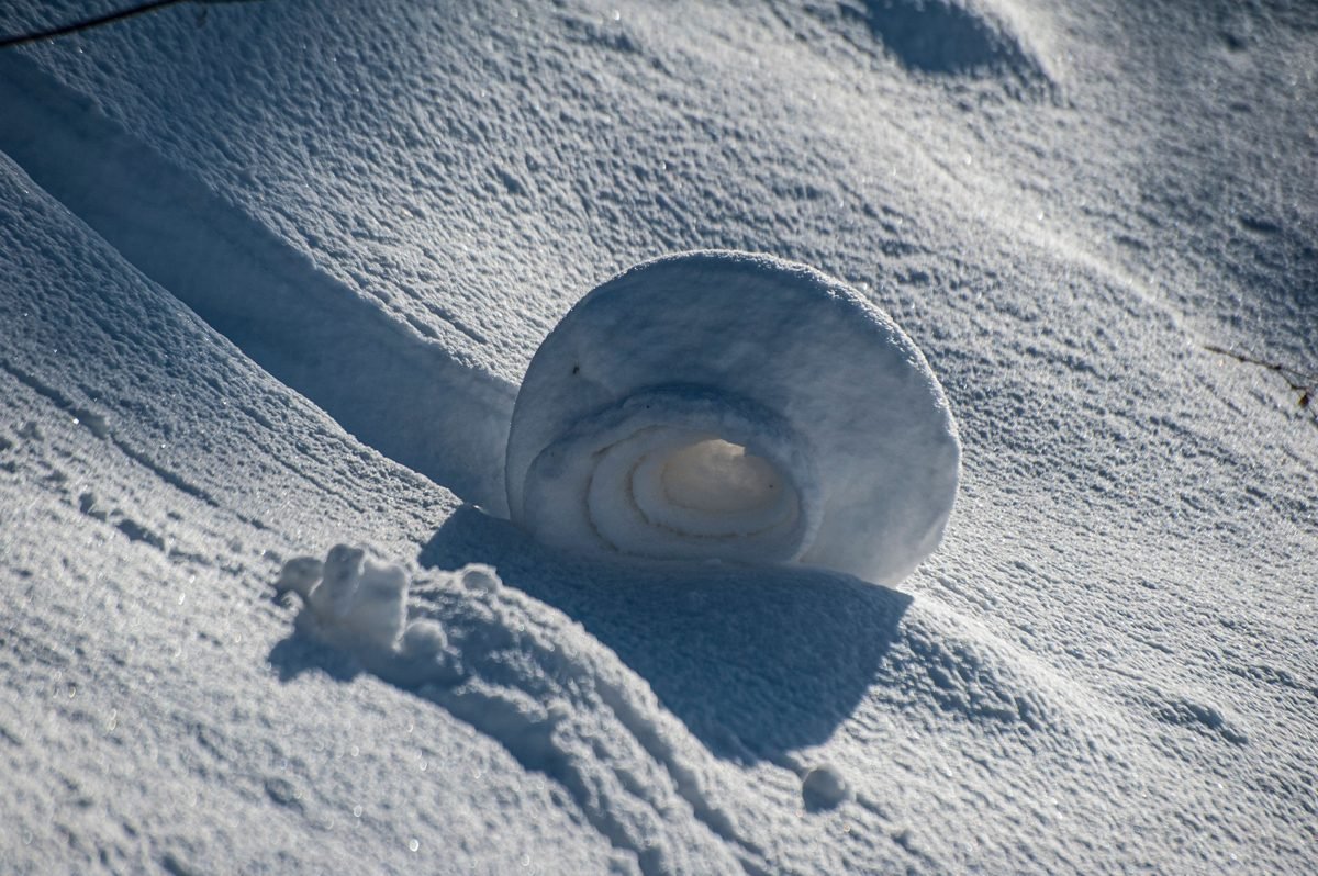 Rolo de neve formado naturalmente em uma encosta nevada, metáfora visual da bola de neve crescendo