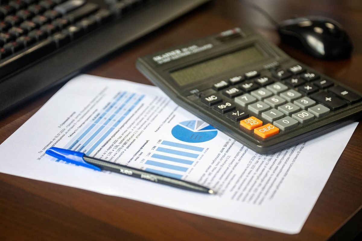 Mesa de trabalho com relatório financeiro com gráficos de barras e pizza, calculadora e caneta