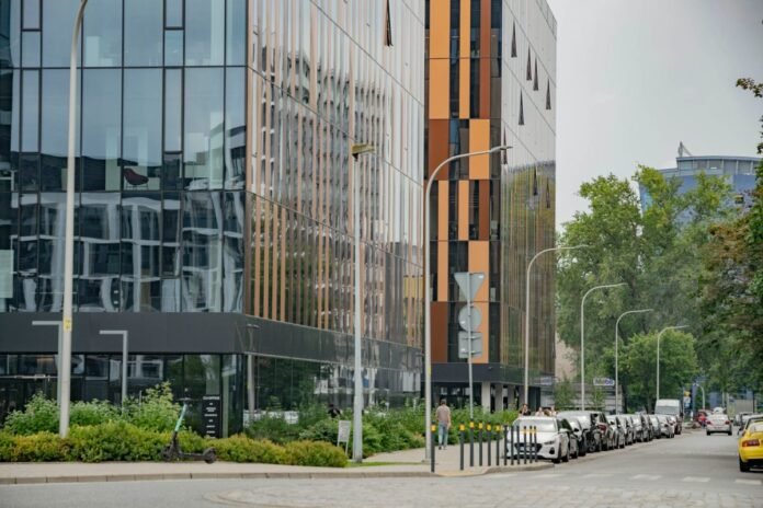 Edifício comercial moderno de escritórios com fachada de vidro e painéis alaranjados, em rua com árvores