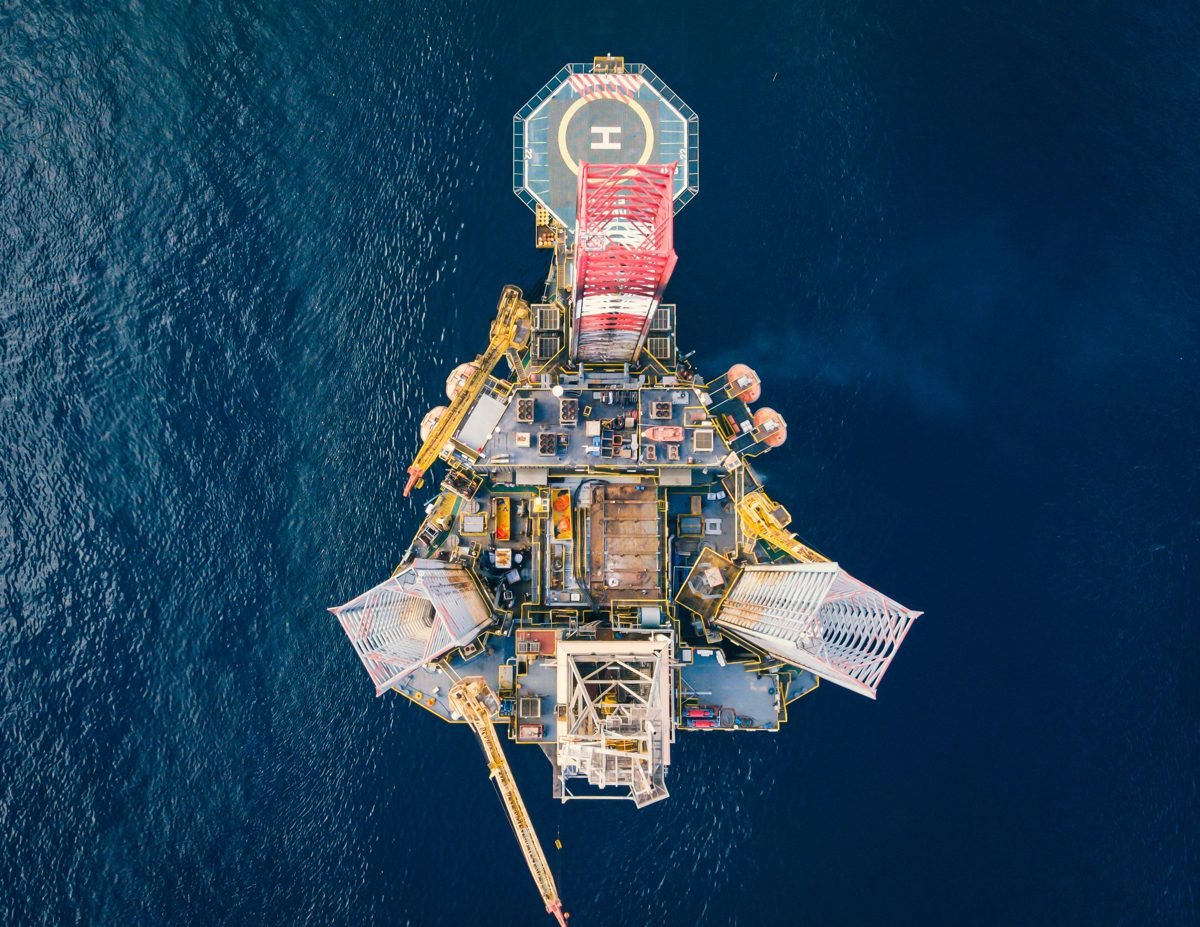 Vista aérea de plataforma de exploração de petróleo em alto mar, com heliponto, cercada por água azul profunda