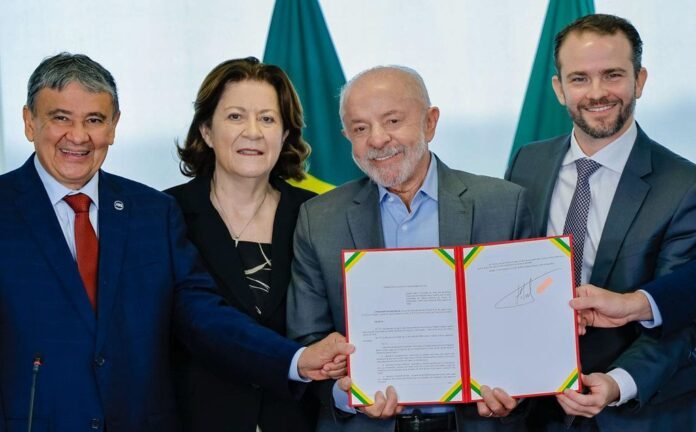 Presidente Luiz Inácio Lula da Silva sorri ao lado de ministros, segurando um decreto assinado, durante anúncio sobre o reajuste do Bolsa Família no Palácio do Planalto